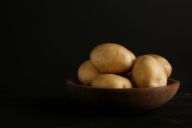 Fresh organic potatoes in bowl and space for text on black background