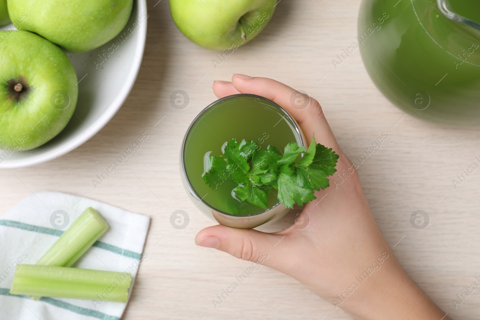 Photo of Woman holding glass of fresh celery juice at white table, top view