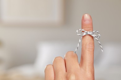 Photo of Woman showing index finger with tied bow as reminder on blurred background, closeup. Space for text