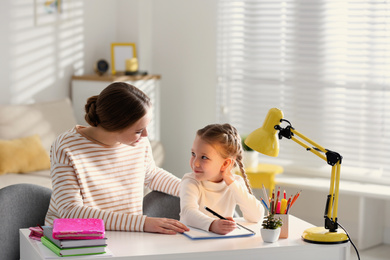 Photo of Woman helping her daughter with homework at table indoors