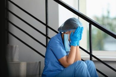 Exhausted doctor sitting on stairs in hospital, space for text