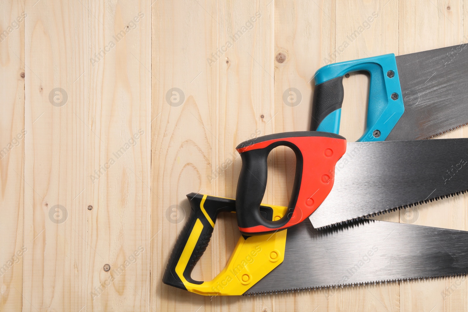 Photo of Saws with colorful handles on wooden background, flat lay. Space for text