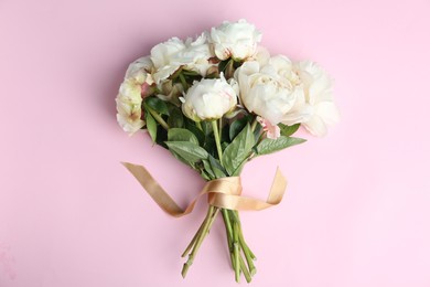 Bouquet of beautiful peonies with ribbon on pink background, flat lay
