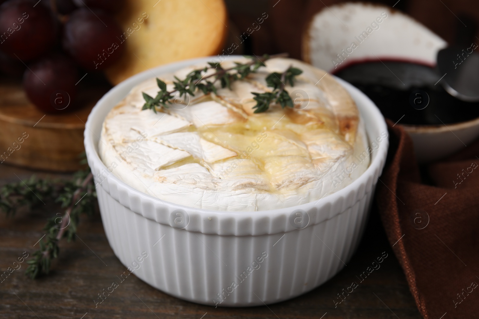 Photo of Tasty baked camembert and thyme in bowl on wooden table, closeup