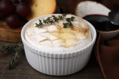 Tasty baked camembert and thyme in bowl on wooden table, closeup