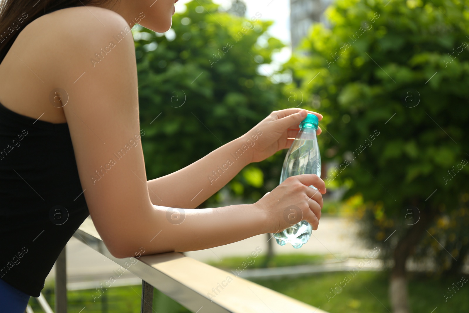 Photo of Young woman with bottle of pure water outdoors, closeup