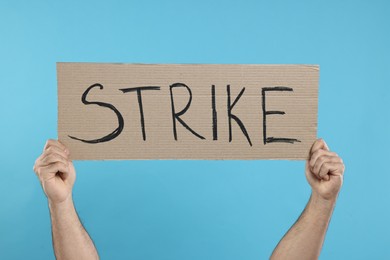 Photo of Man holding cardboard banner with word Strike on light blue background, closeup