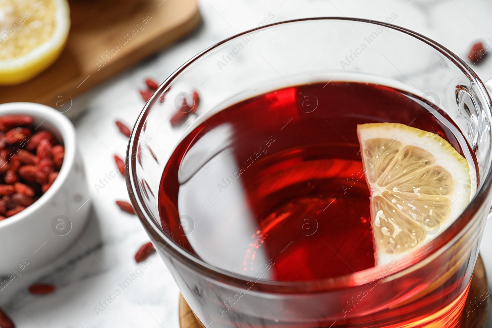 Photo of Healthy goji tea with lemon in glass cup on table, closeup