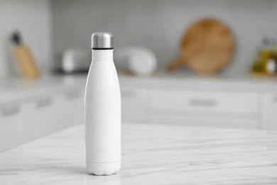 Photo of Stylish thermo bottle on white table in kitchen. Space for text