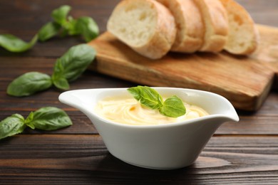 Tasty sauce with basil leaves in gravy boat on wooden table