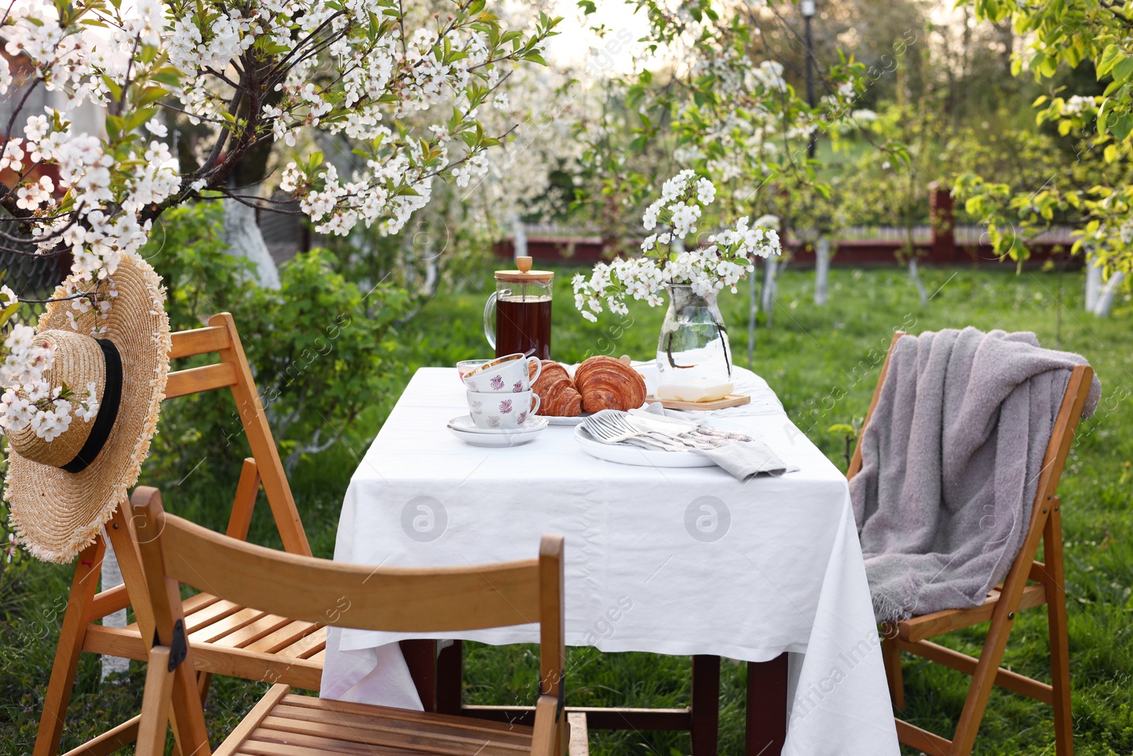 Photo of Stylish table setting with beautiful spring flowers, tea and croissants in garden