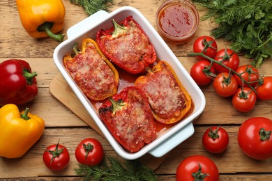 Photo of Tasty stuffed peppers in dish and ingredients on wooden table, flat lay