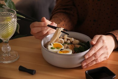 Photo of Woman eating delicious ramen with chopsticks at wooden table, closeup. Noodle soup