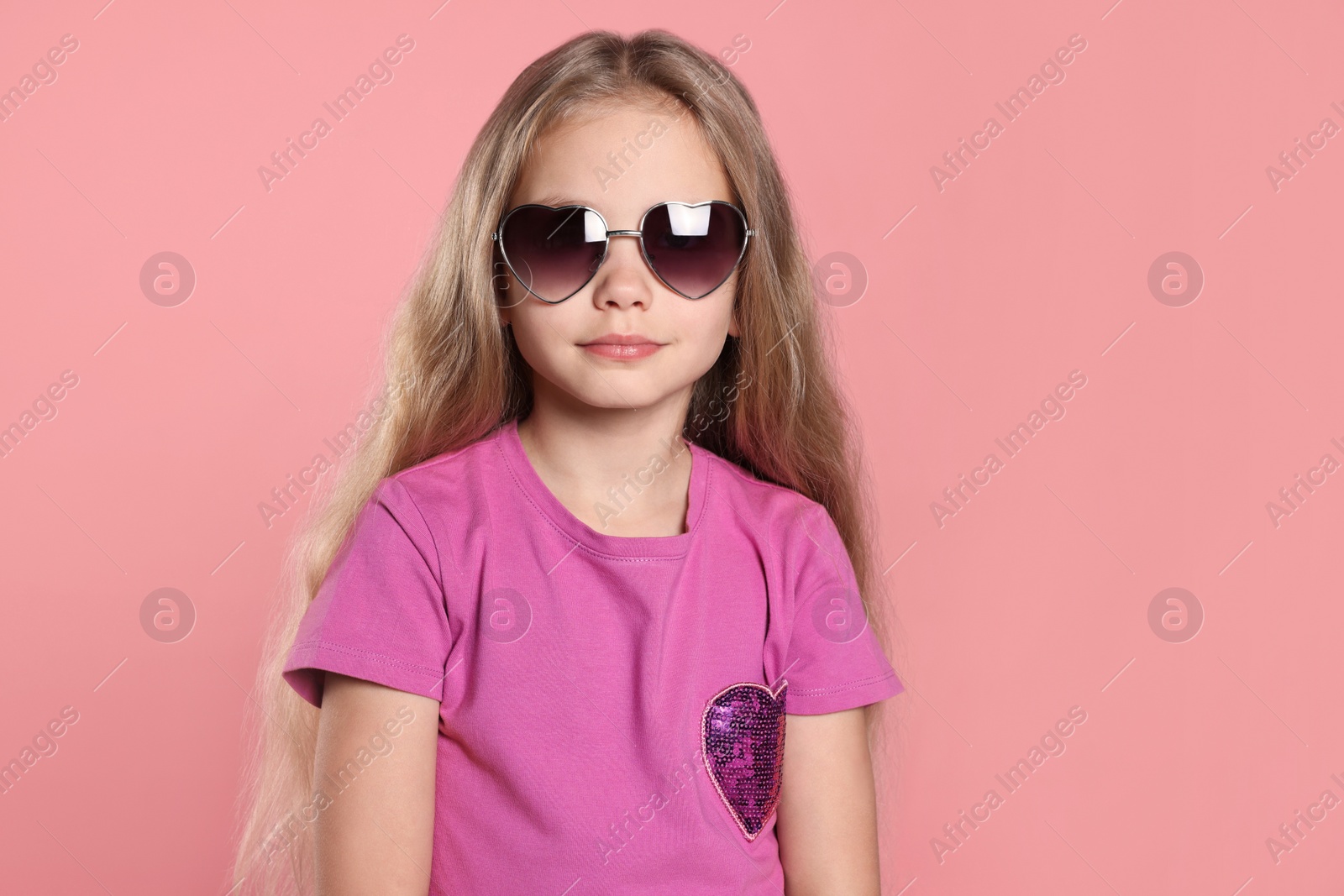 Photo of Girl wearing stylish sunglasses in shape of hearts on pink background