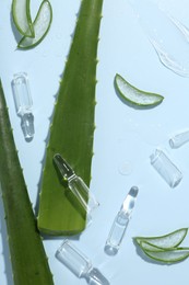 Flat lay composition with skincare ampoules and aloe leaves on light blue background