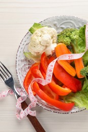 Photo of Healthy diet. Plate of fresh vegetables, measuring tape and fork on light wooden table, top view