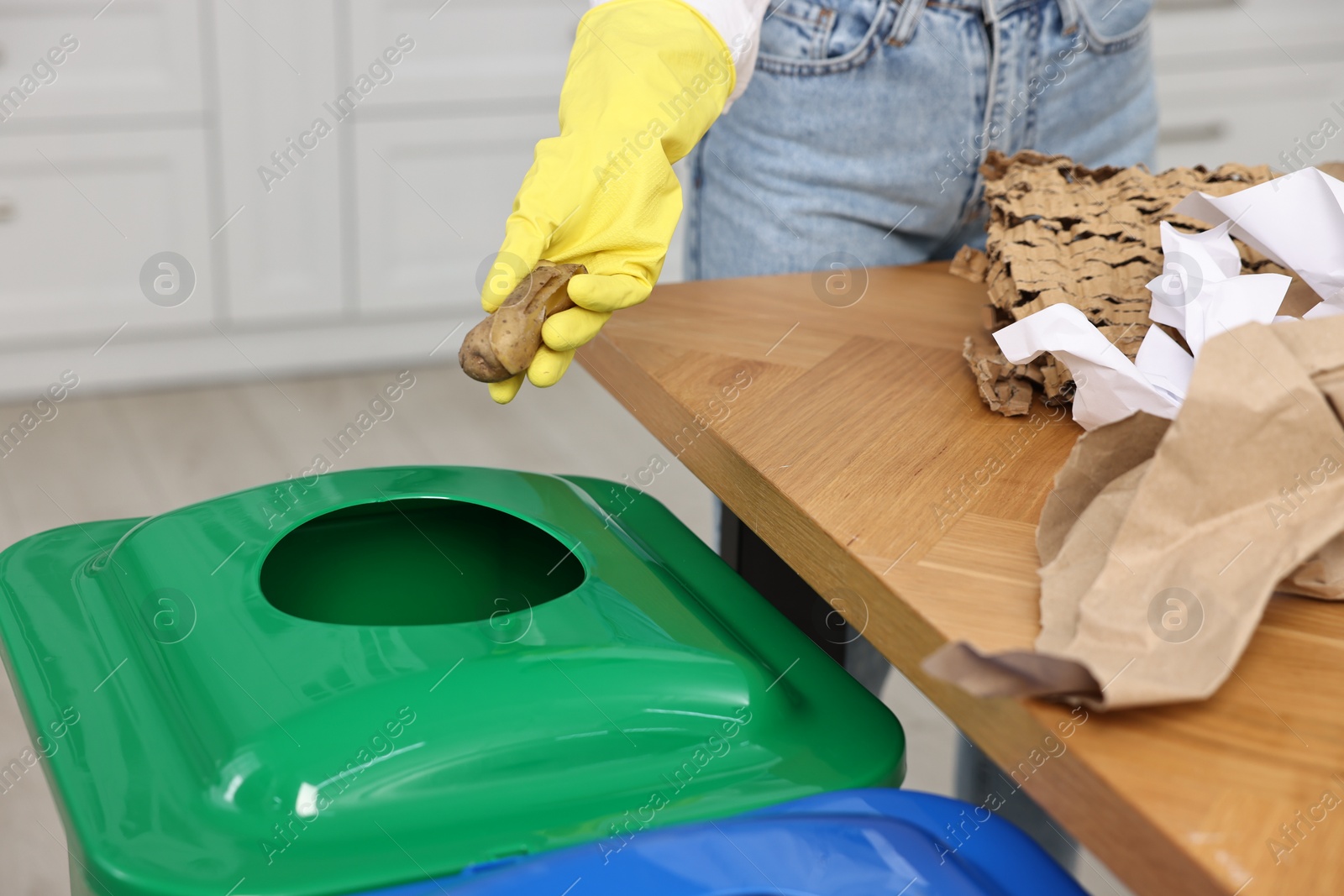 Photo of Garbage sorting. Woman throwing potato peel into trash bin indoors, closeup