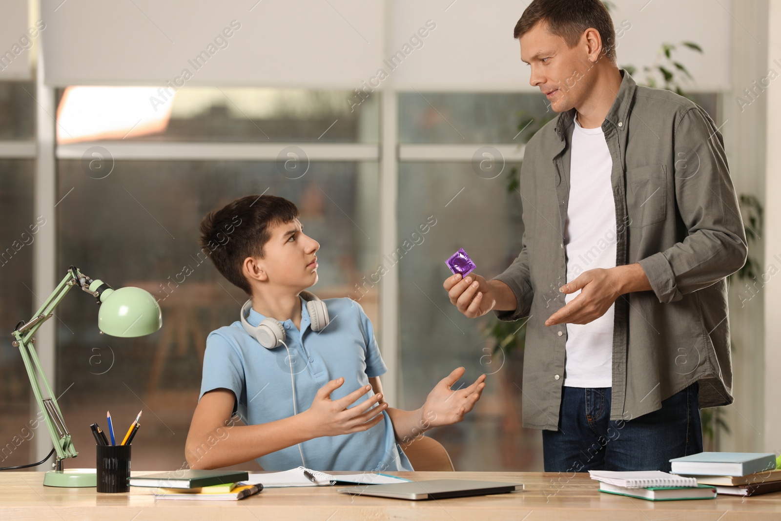 Photo of Father talking with his teenage son about contraception while he doing homework at home. Sex education concept