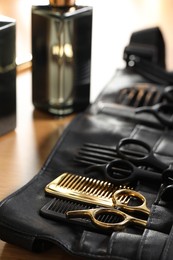 Hairdresser tools. Professional scissors and combs in leather organizer on wooden table, closeup