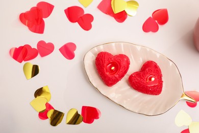 Photo of Red heart shaped candles and confetti on white table, flat lay. Valentine's Day celebration