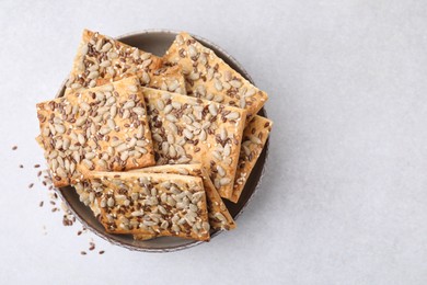 Photo of Cereal crackers with flax, sunflower and sesame seeds in bowl on light textured table, top view. Space for text