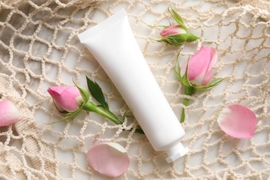 Photo of Tubehand cream and roses in net bag on table, flat lay