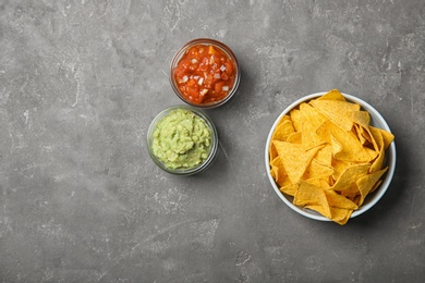 Delicious mexican nachos chips in bowl served with sauces on grey table, flat lay. Space for text