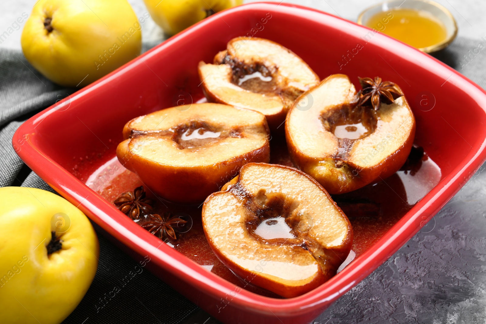 Photo of Tasty baked quinces with honey in dish on grey textured table, closeup