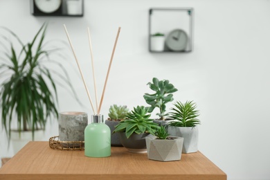 Photo of Air reed freshener and beautiful houseplants on wooden table indoors