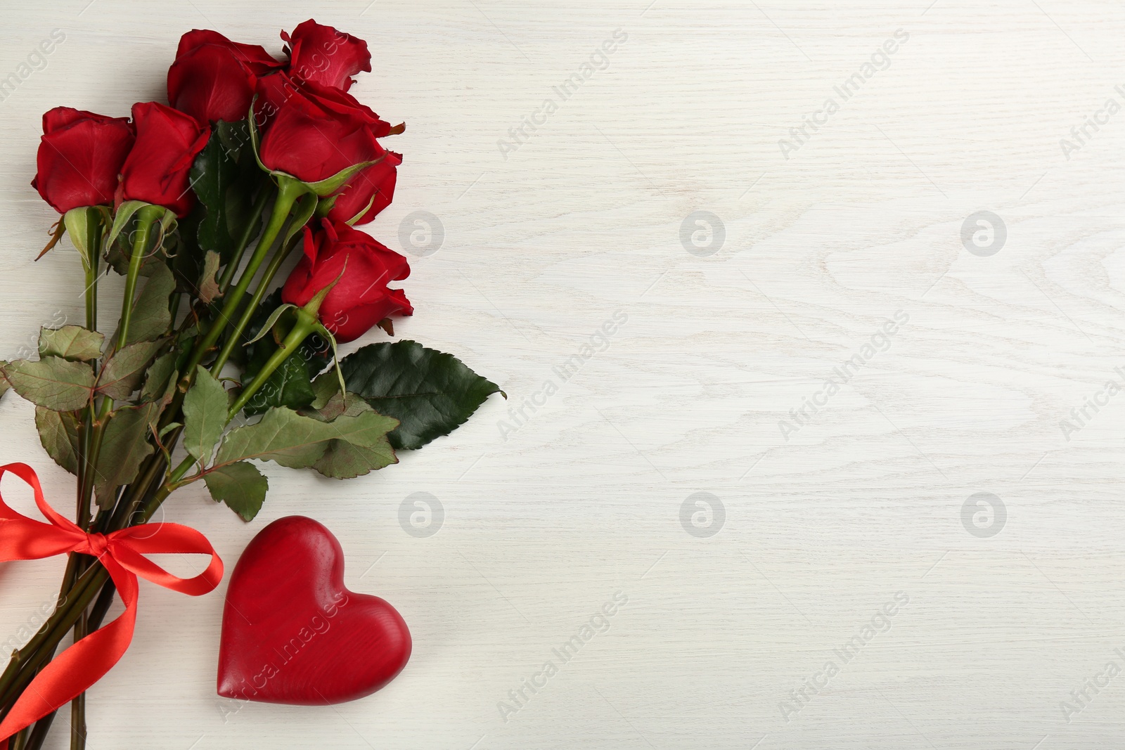 Photo of Beautiful red roses and decorative heart on white wooden background, flat lay with space for text. Valentine's Day celebration