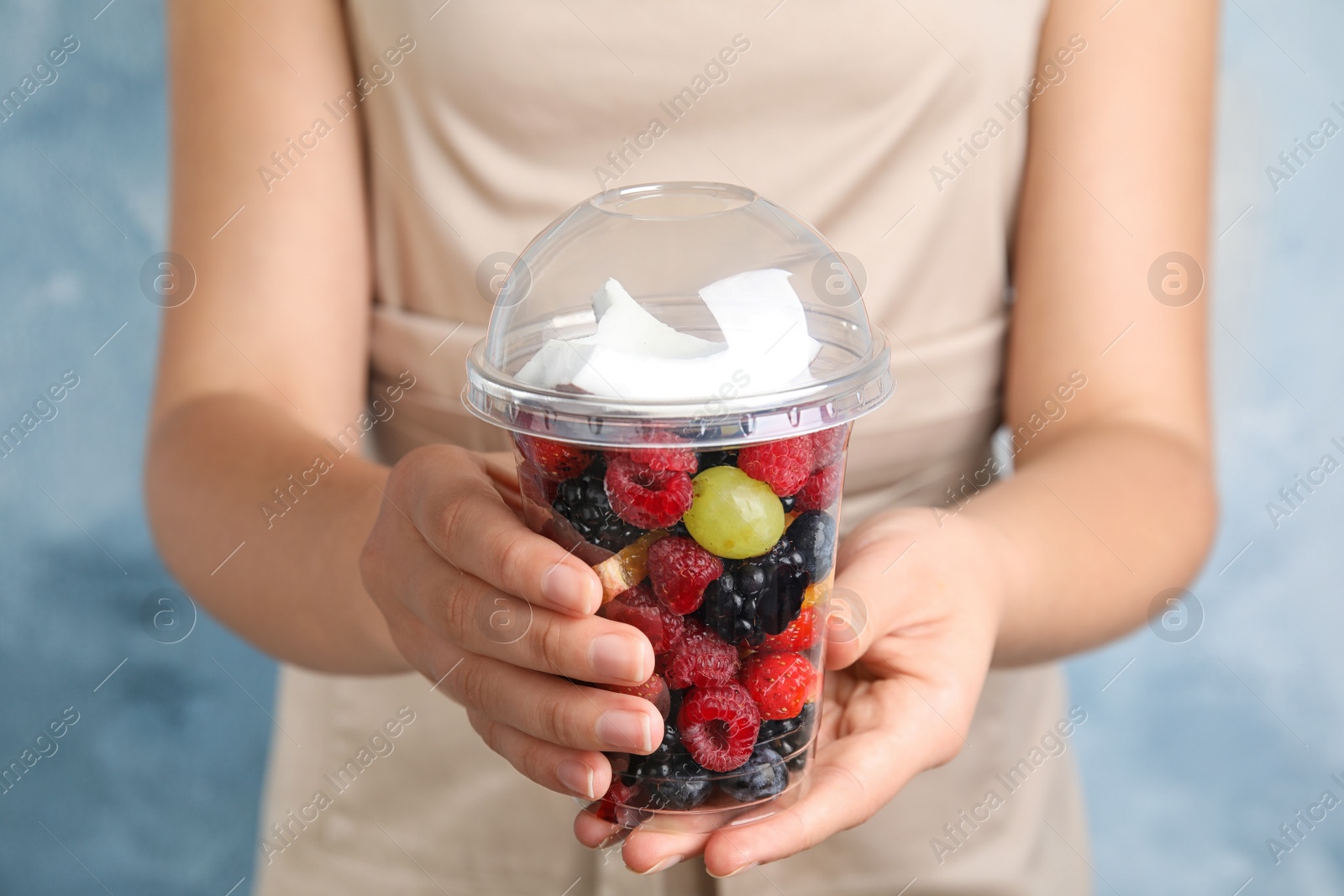 Photo of Woman holding plastic cup with fresh tasty fruit salad against light blue background, closeup