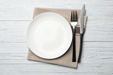 Photo of Stylish ceramic plate, napkin and cutlery on white wooden background, flat lay