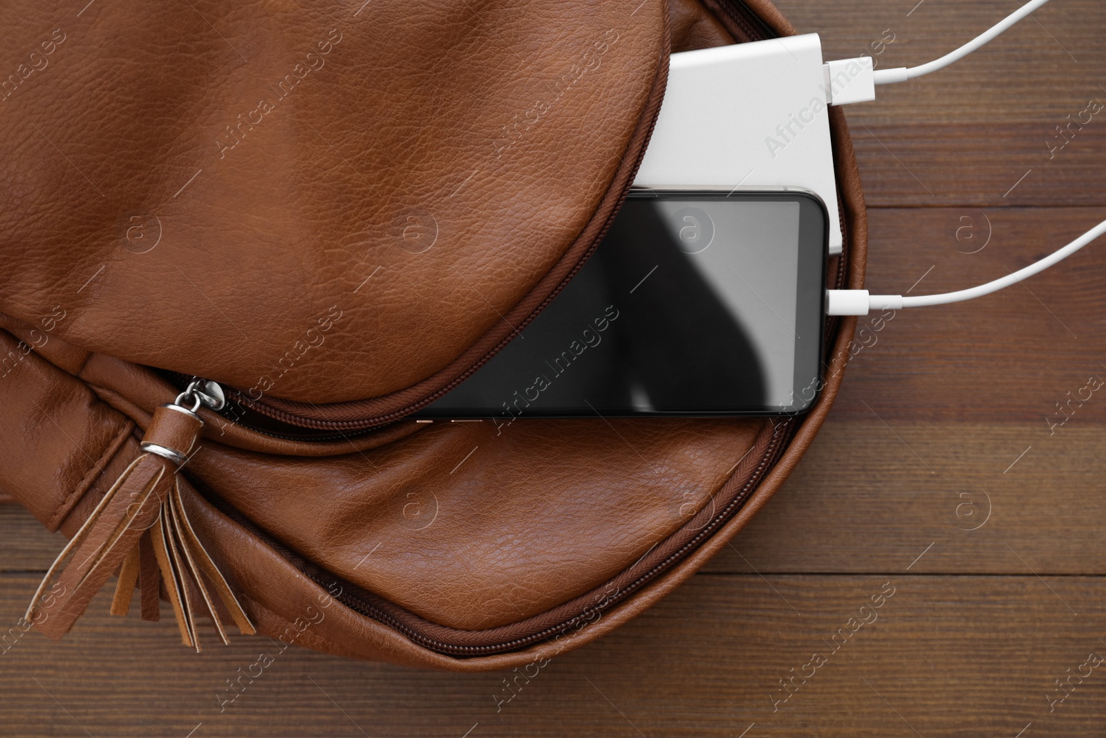 Photo of Charging mobile phone with power bank in backpack on wooden table, top view