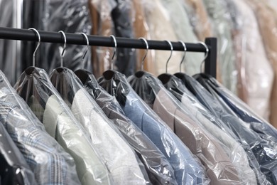 Dry-cleaning service. Many different clothes in plastic bags hanging on rack indoors, closeup