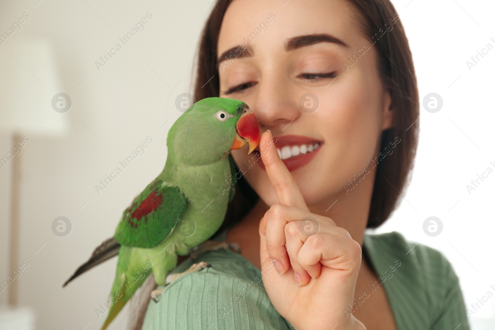 Photo of Young woman with Alexandrine parakeet indoors. Cute pet