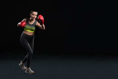 Photo of Beautiful woman in boxing gloves training on black background. Space for text