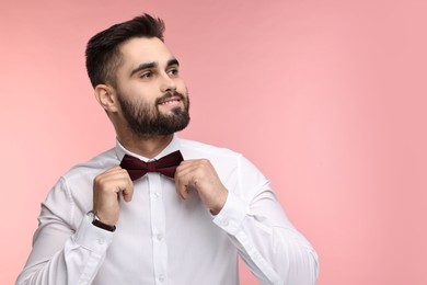 Photo of Portrait of smiling man adjusting bow tie on pink background. Space for text