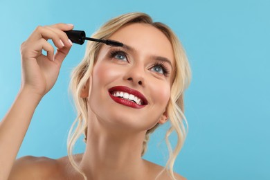 Beautiful makeup. Smiling woman applying mascara on light blue background