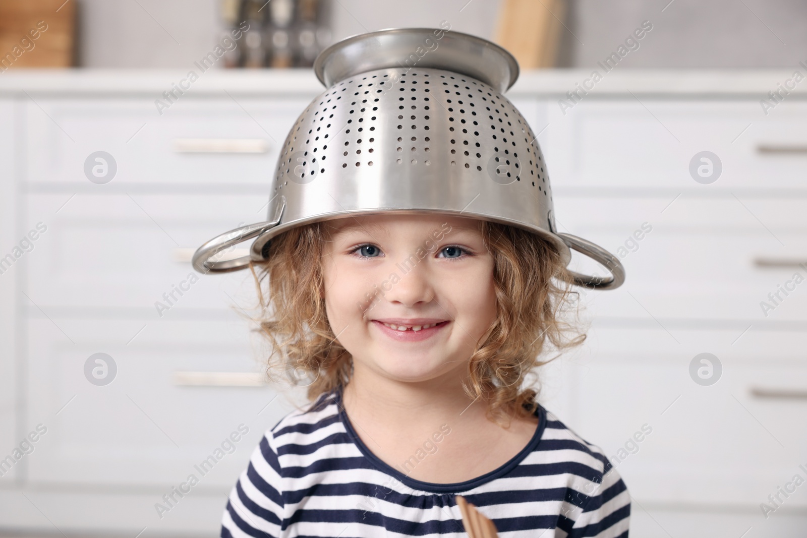 Photo of Cute little girl with colander on her head in kitchen