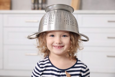 Cute little girl with colander on her head in kitchen