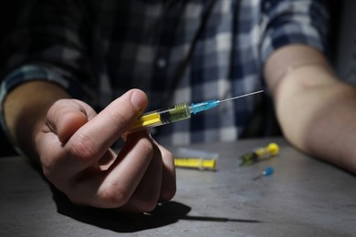 Photo of Drug addiction. Man with syringe at grey table, closeup
