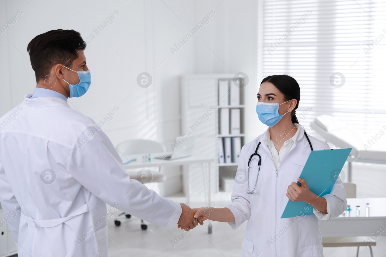 Photo of Doctors with protective masks giving handshake in clinic