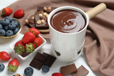 Photo of Fondue pot with chocolate and different berries on white wooden table