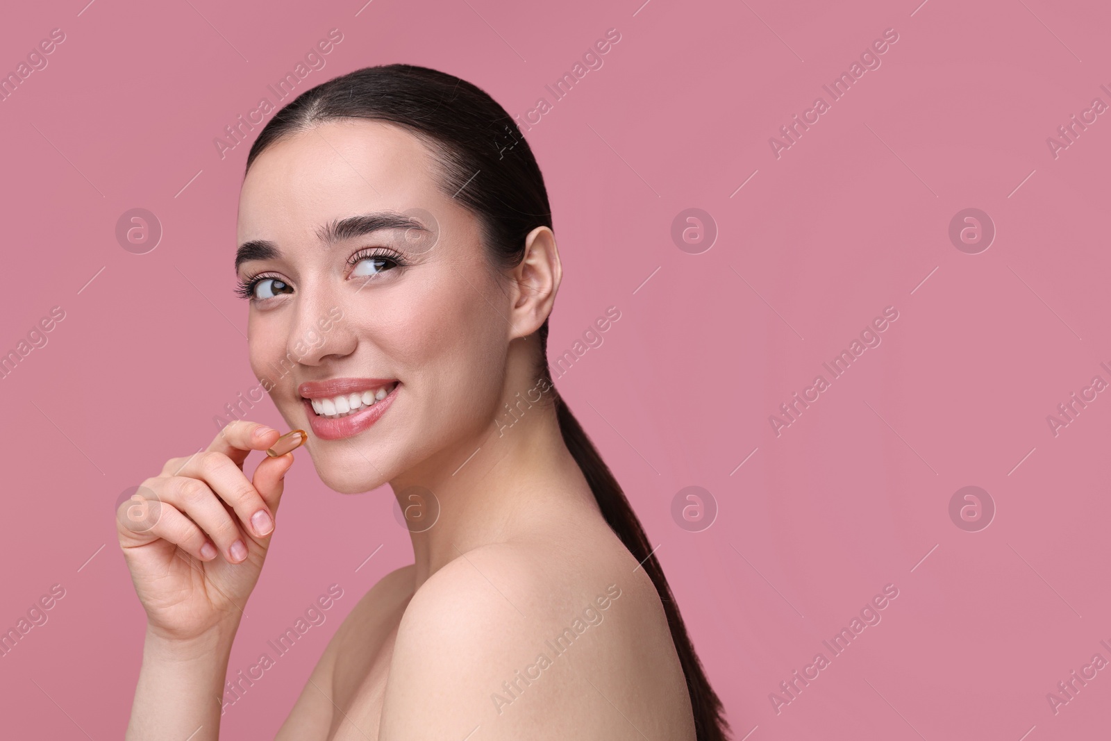 Photo of Beautiful young woman with vitamin pill on pink background. Space for text