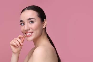 Photo of Beautiful young woman with vitamin pill on pink background. Space for text