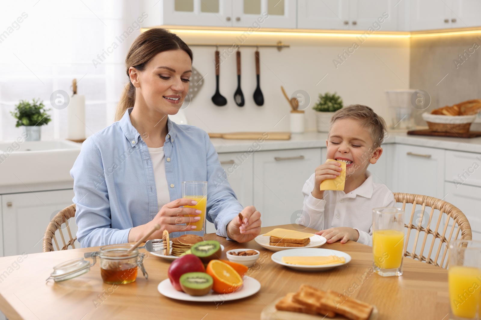 Photo of Mother and her cute little son having breakfast at table in kitchen