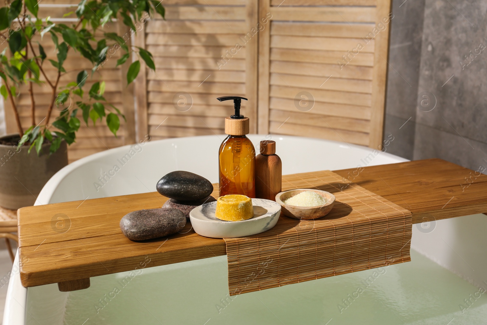 Photo of Wooden tray with spa products and stones on bath tub in bathroom