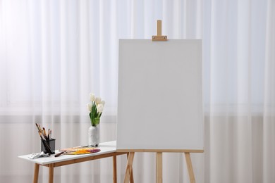 Photo of Wooden easel with canvas and art supplies on table indoors. Space for text