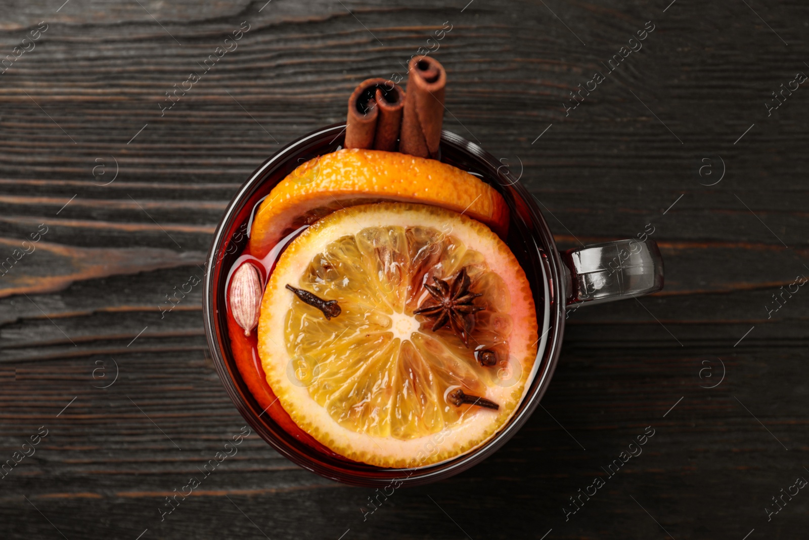 Photo of Glass cup of tasty mulled wine on black wooden table, top view