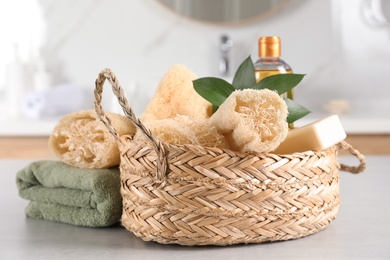 Photo of Natural loofah sponges in wicker basket and towel on table indoors